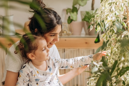 woman with her little daughter is looking at indoor plants at home